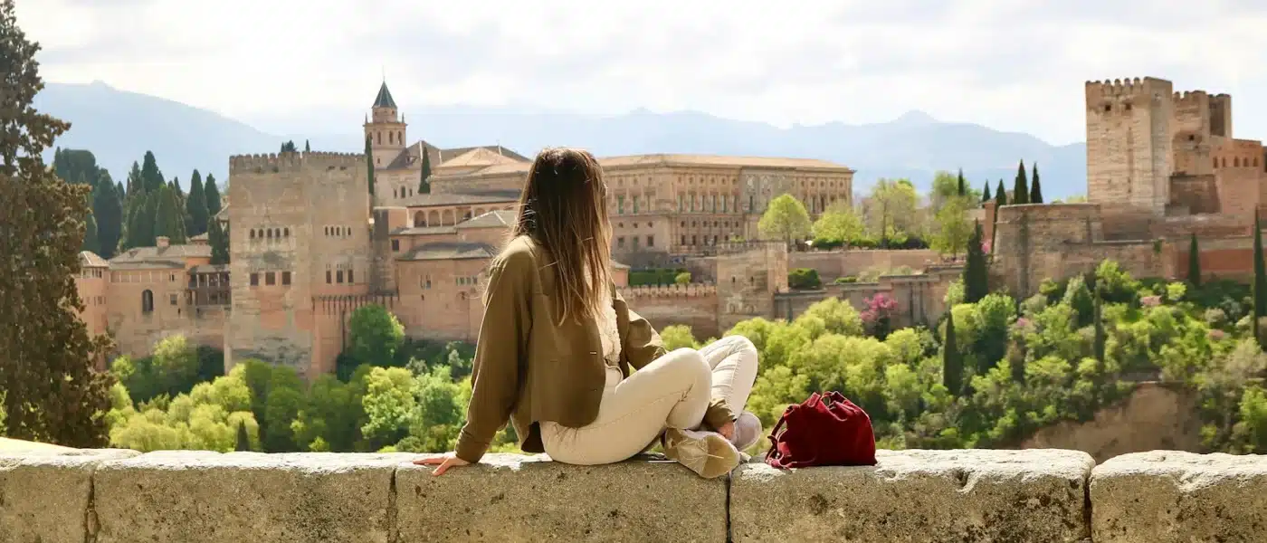 woman in beige long sleeve shirt sitting on gray concrete bench during daytime - granada