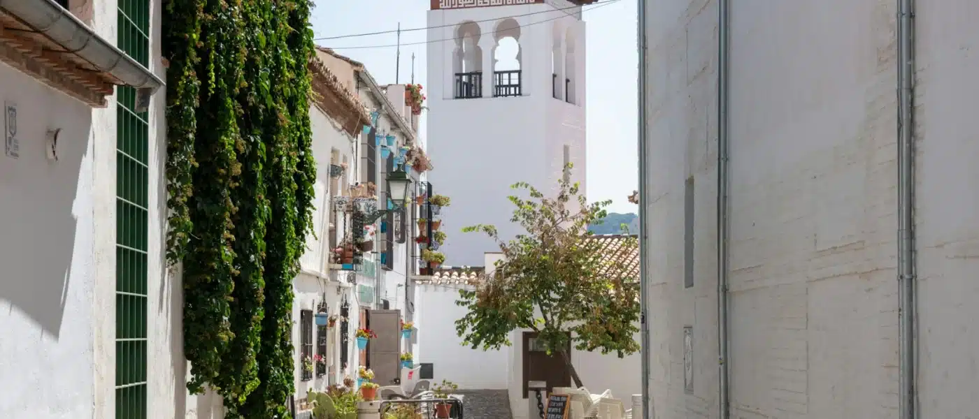 A narrow street with a clock tower in the background, Granada