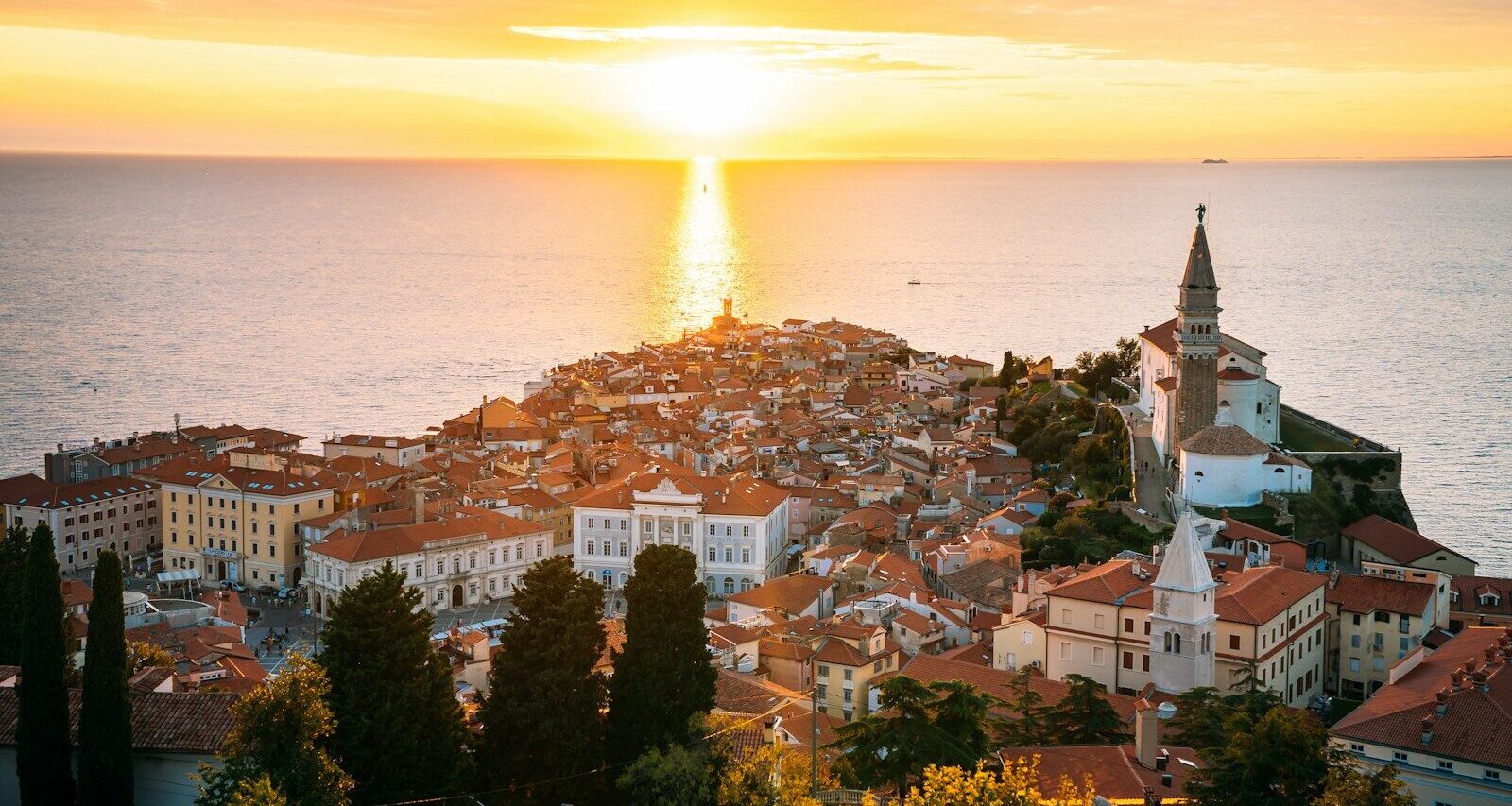 the sun is setting over a city by the ocean