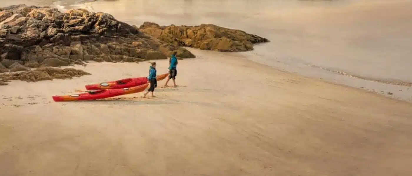 Kayaks drifting calmly outside a sea arch at golden hour