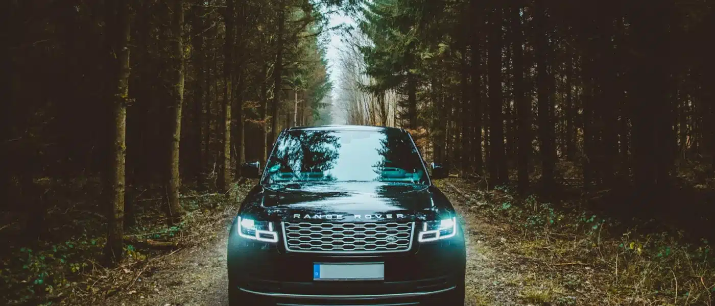 green Land Rover Range Rover SUV passing on dirt road between green trees